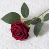 A deep red artificial rose bloom on a green stem with leaves, set against a white textured background.