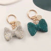 A pair of sparkling rhinestone bow keychains, one silver and one teal green.