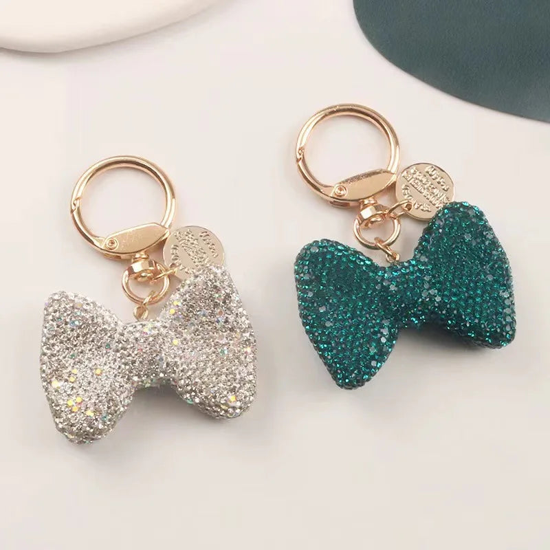 A pair of sparkling rhinestone bow keychains, one silver and one teal green.
