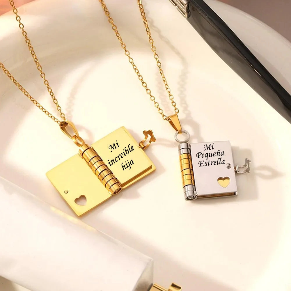 Gold and silver openable book pendant necklace with an engraved message on a white background.