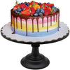 A layered cake with pink, yellow, and blue frosting and a chocolate drip, topped with fresh berries, displayed on a black met