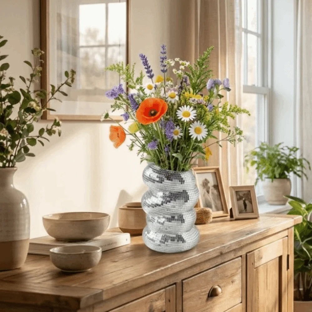 A light gray spiral vase filled with colorful wildflowers sits on a wooden cabinet top.