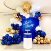 A display of round latex balloons in gold, white, and blue clustered around a blue backdrop for a party theme.