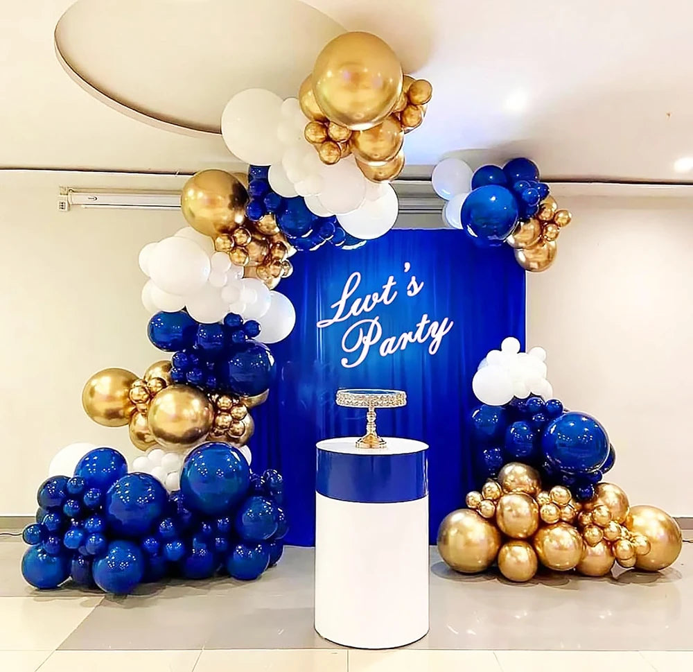 A display of round latex balloons in gold, white, and blue clustered around a blue backdrop for a party theme.