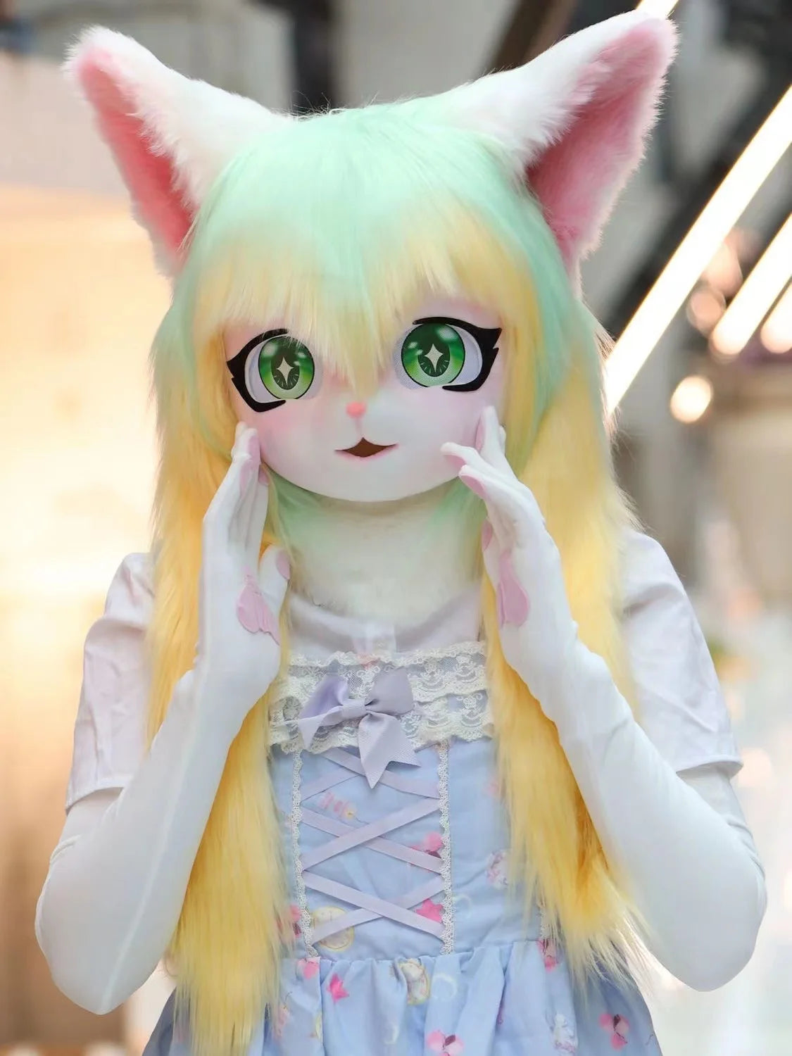 A cute, light green and yellow furry cosplay head with large eyes and pink ears, wearing a light blue dress.
