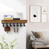 A rustic wooden floating shelf with hooks mounted on a white wall above a sofa.