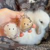A hand holds a clear plastic rabbit hair keepsake keychain next to a white fluffy rabbit.