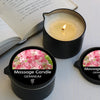 A black jar of Geranium massage candle with a lit wick sits next to an open book.
