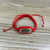 A red beaded bracelet with a rectangular, carved wooden charm featuring colorful inlay.