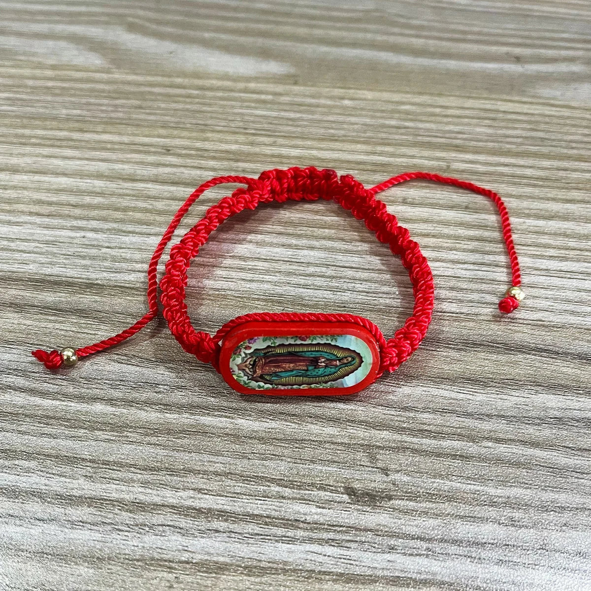 A red beaded bracelet with a rectangular, carved wooden charm featuring colorful inlay.