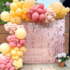 A vibrant pink and yellow balloon arch backdrop featuring shimmering sequins for a party decoration.