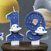 Two glittery blue planet number candles, 1 and 0, with white moon accents, displayed on a wooden surface.