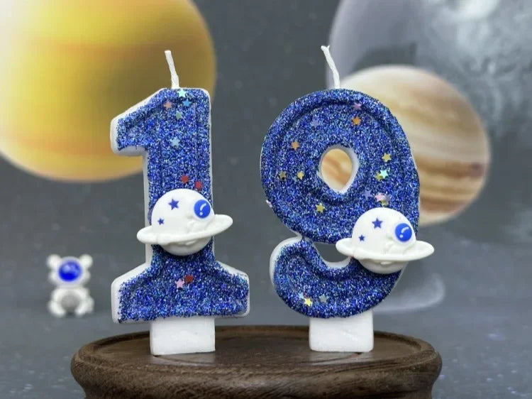 Two glittery blue planet number candles, 1 and 0, with white moon accents, displayed on a wooden surface.