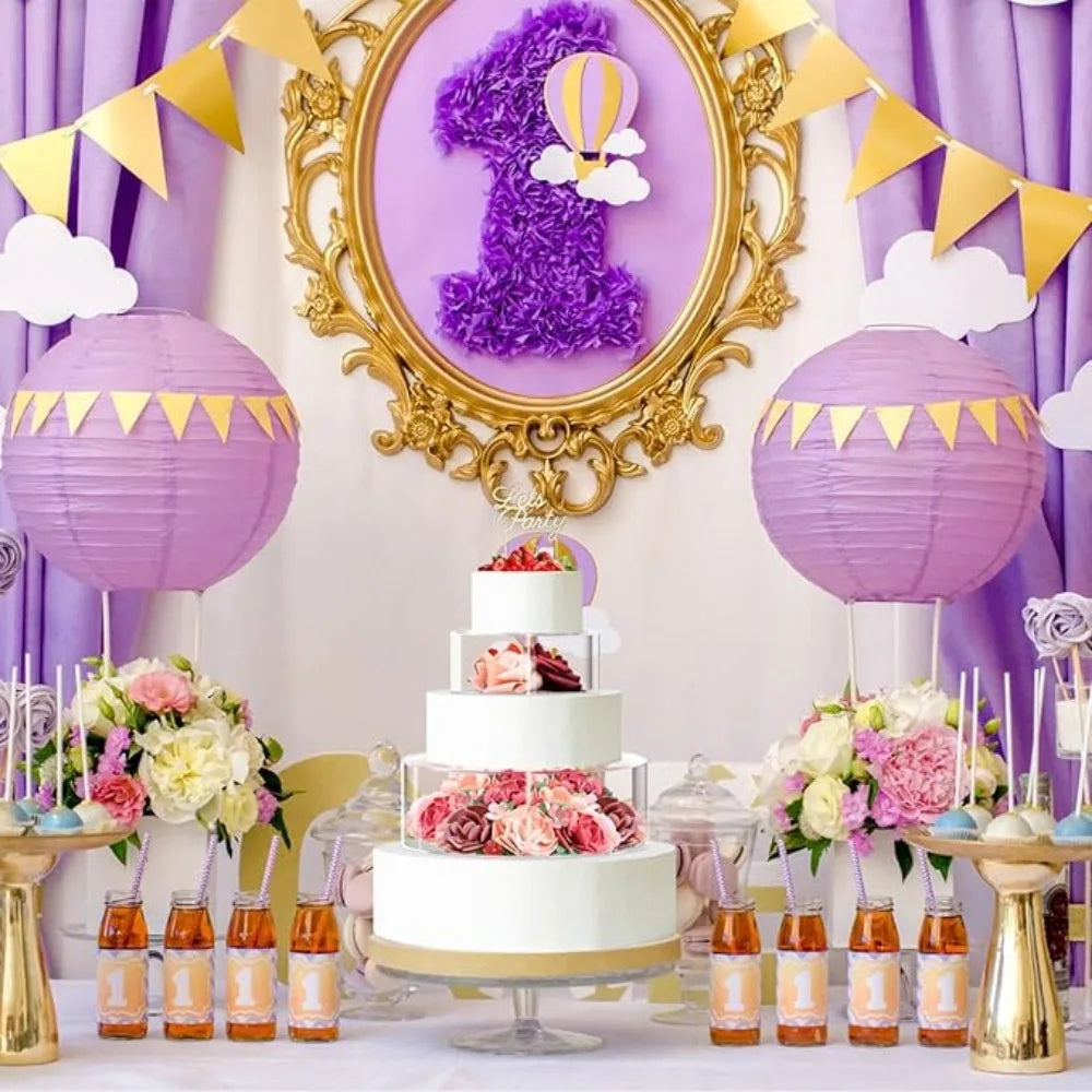 A tiered white and pink cake display with purple accents set on a table surrounded by clear acrylic stands.