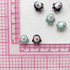 A collection of small resin penguin figurines in white and teal colors arranged on a pink ruler.