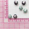 A collection of small resin penguin figurines arranged on a white background next to a ruler.