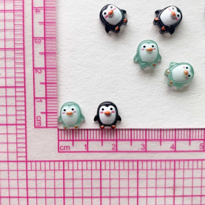 A collection of small resin penguin figurines arranged on a white background next to a ruler.