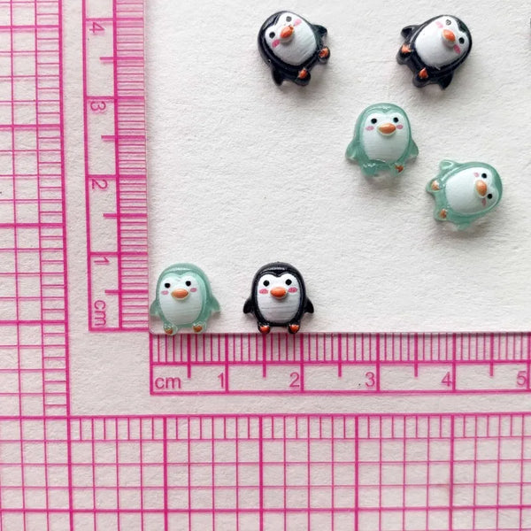 A collection of small resin penguin figurines arranged on a white background next to a ruler.