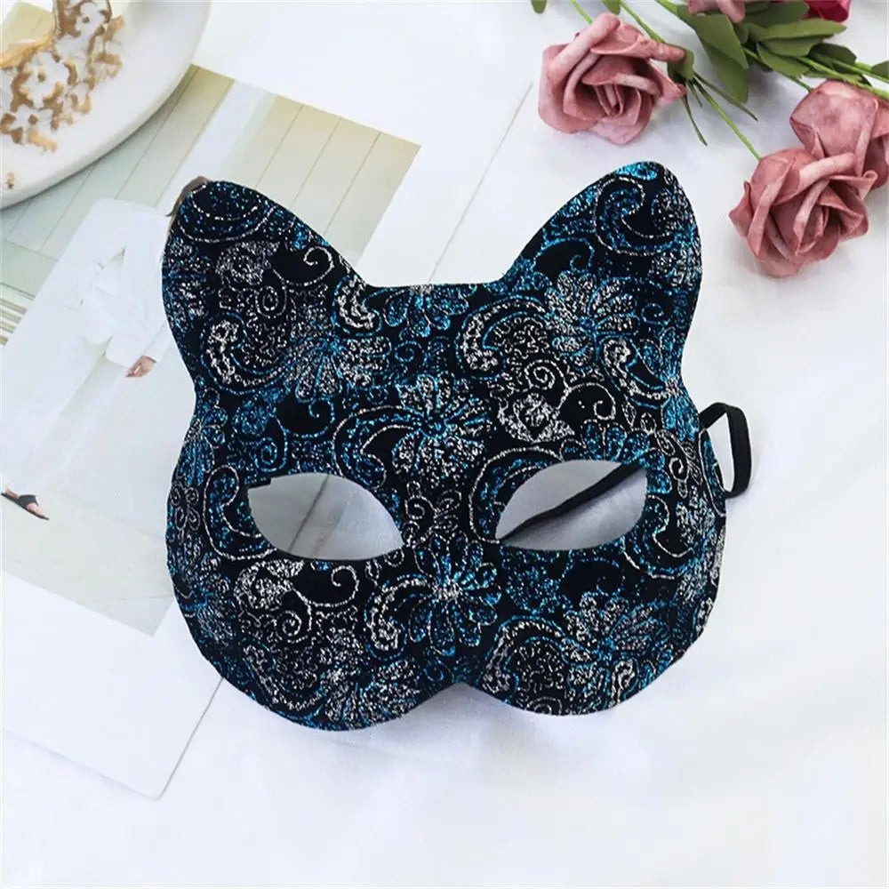 A black lace half-face mask with blue and white floral patterns is displayed on a white surface next to pink roses.