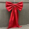 A vibrant red satin bow with a long tulle drape hanging against a gray wall.