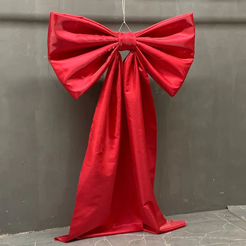 A vibrant red satin bow with a long tulle drape hanging against a gray wall.