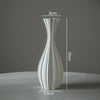 A tall, slender, white ceramic-style vase with a curved, ribbed texture shown against a gray background.