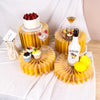 A decorative buffet riser set featuring yellow acrylic stands displaying cakes, fruit, and a bottle.