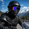 A person wearing a black full face helmet and goggles is riding an offroad motorcycle on a scenic mountain road.