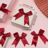 A display of elegant red satin ribbon bows for gift wrapping and decor, shown on a pink background.