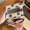 A hand holds a beige canvas travel makeup bag with a mirror and a zippered compartment on a wooden table.