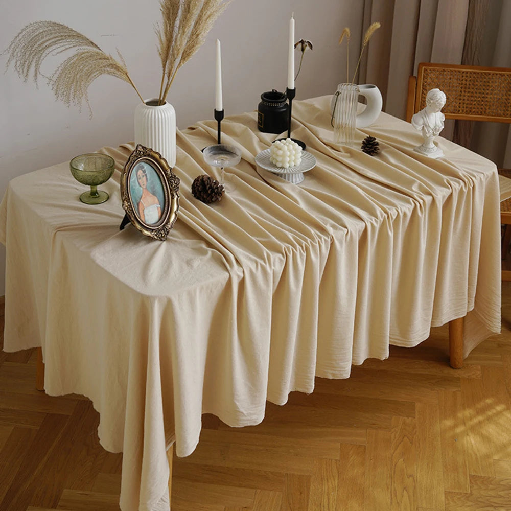 A beige cotton rectangle tablecloth set for dining or events, decorated with dried grasses and candles.
