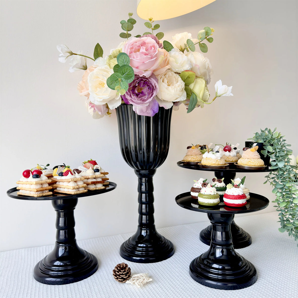 A black pedestal vase holds a lush arrangement of pink and white roses and greenery for a centerpiece display.
