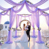 An elegant purple tulle backdrop decorated with flowers framing a couple for an event.