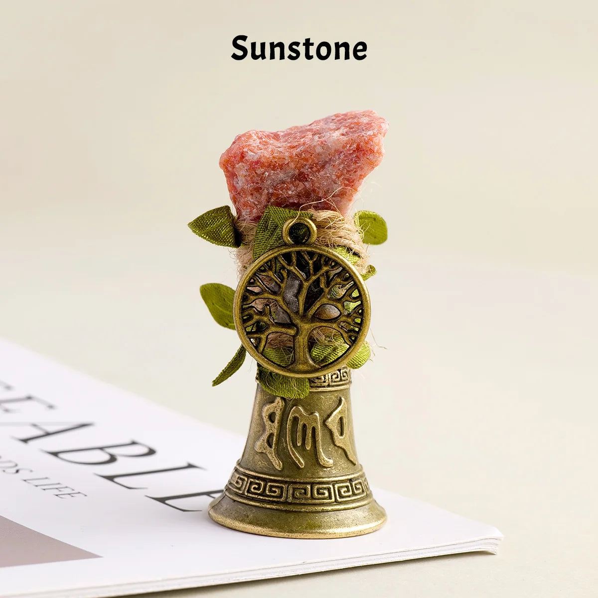 A piece of pink and orange Sunstone crystal mounted on a brass bell with a copper finish.