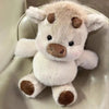 A fluffy white Highland cow plush toy with brown markings sitting on a light-colored surface.