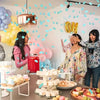 A woman is celebrating a gender reveal with confetti and balloons in a bright room.