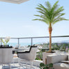 An artificial golden palm tree stands in an outdoor setting with a view of the sea and city landscape.