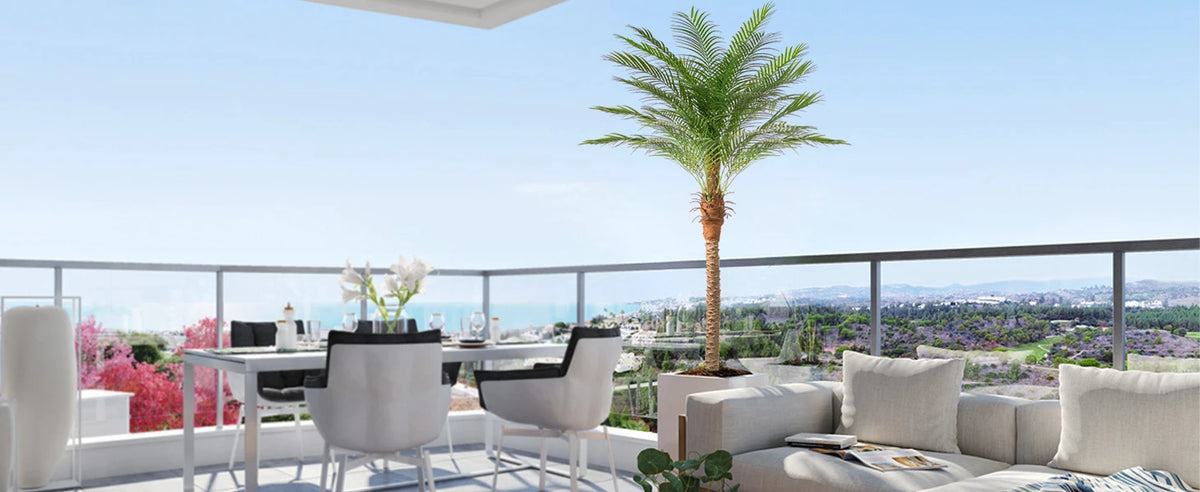 An artificial golden palm tree stands in an outdoor setting with a view of the sea and city landscape.