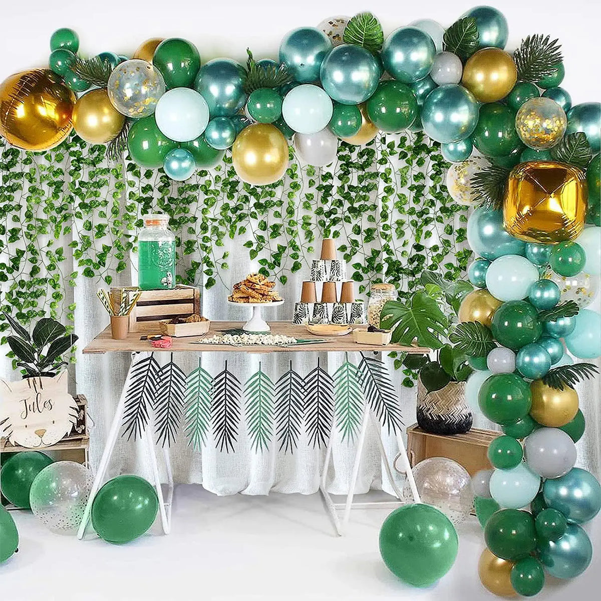 A festive holiday display featuring a green and gold ivy leaf garland backdrop with round ornaments.