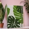 Vertikaler Fotoalbum-Cover mit großen grünen Monstera-Blättern auf weißem Hintergrund und grauem Einband.