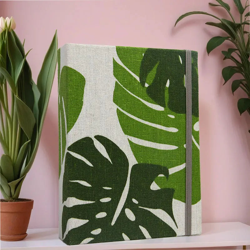 Vertikaler Fotoalbum-Cover mit großen grünen Monstera-Blättern auf weißem Hintergrund und grauem Einband.
