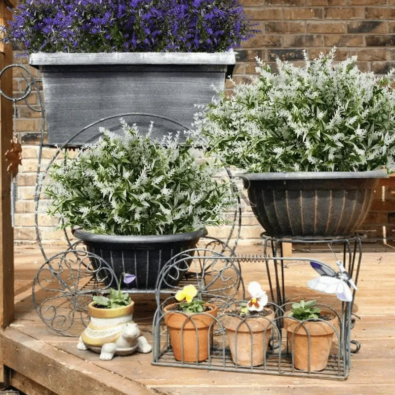 A collection of artificial flowers and greenery in various pots and planters on a wooden surface.