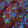 Una mano sostiene una pila de 50 adornos de uñas en forma de tortuga mini coloridos que brillan con varios colores brillantes