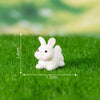 A small white rabbit figurine sitting on green grass with measurement lines.