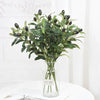Artificial olive leaf branch with dark green leaves and small black berries in a clear glass vase