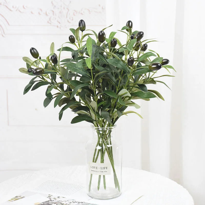 Artificial olive leaf branch with dark green leaves and small black berries in a clear glass vase