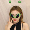 A woman wearing green alien sunglasses with antennae against a light background.