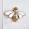 A gold resin animal wall hanging decor shaped like a dragonfly mounted on a white wall.