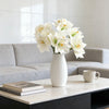 A vase of white artificial clivia amaryllis flowers on a light marble table in a modern living room