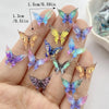 A hand displays a collection of 30 colorful resin butterfly embellishments in various shades of blue, purple, and yellow.